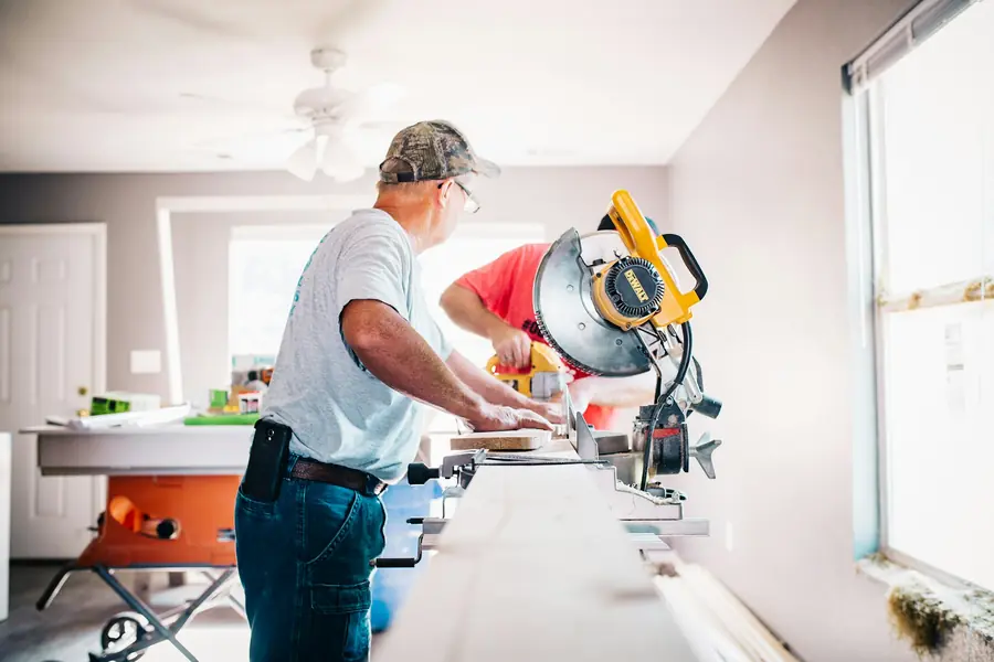 Contractors cutting trim with a miter saw inside a bright room being renovated
