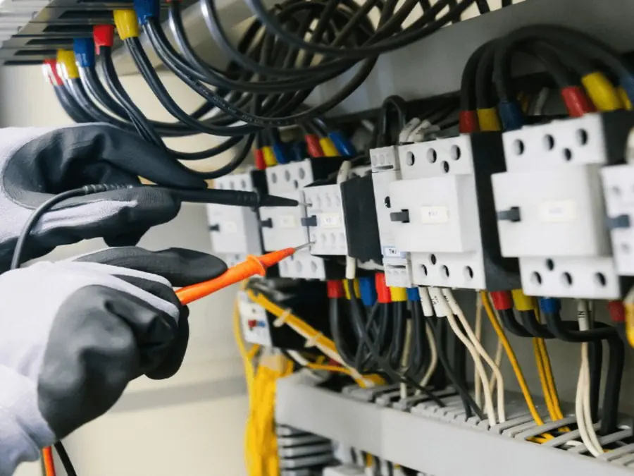 Electrician in insulated gloves testing wiring inside an electrical panel